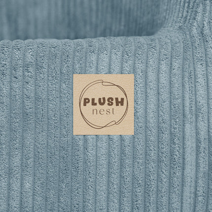 Logo-label van Plush Nest op blauwe fauteuil – merkafwerking op ribstof