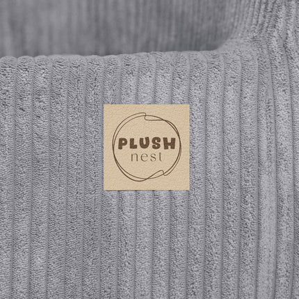 Close-up van Plush Nest logo op grijze kinderfauteuil – merklabel op stof